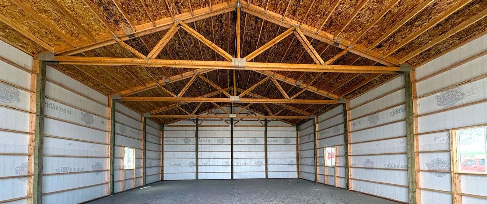 Interior of a completed building shell with exposed timber trusses and a finished concrete floor