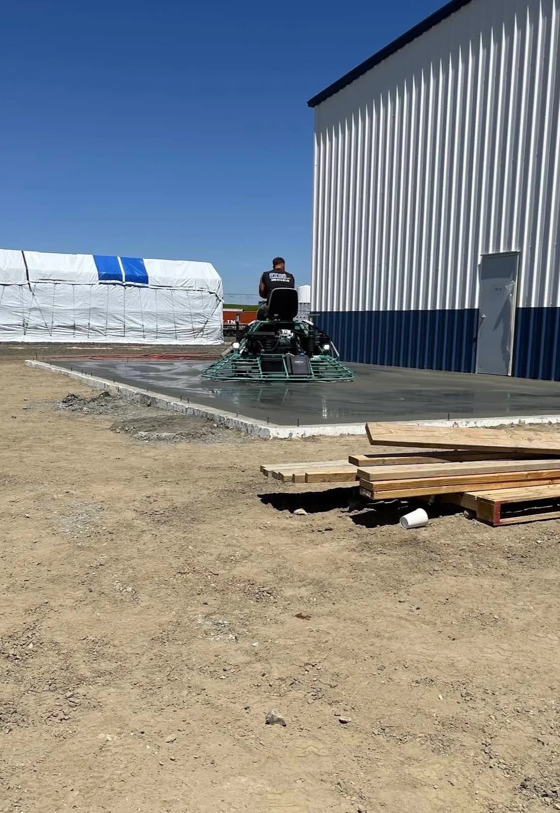 Power trowel finishing a fresh concrete slab beside a steel building