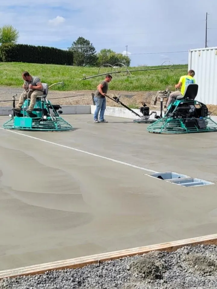 Crew finishing a fresh concrete slab beside a building