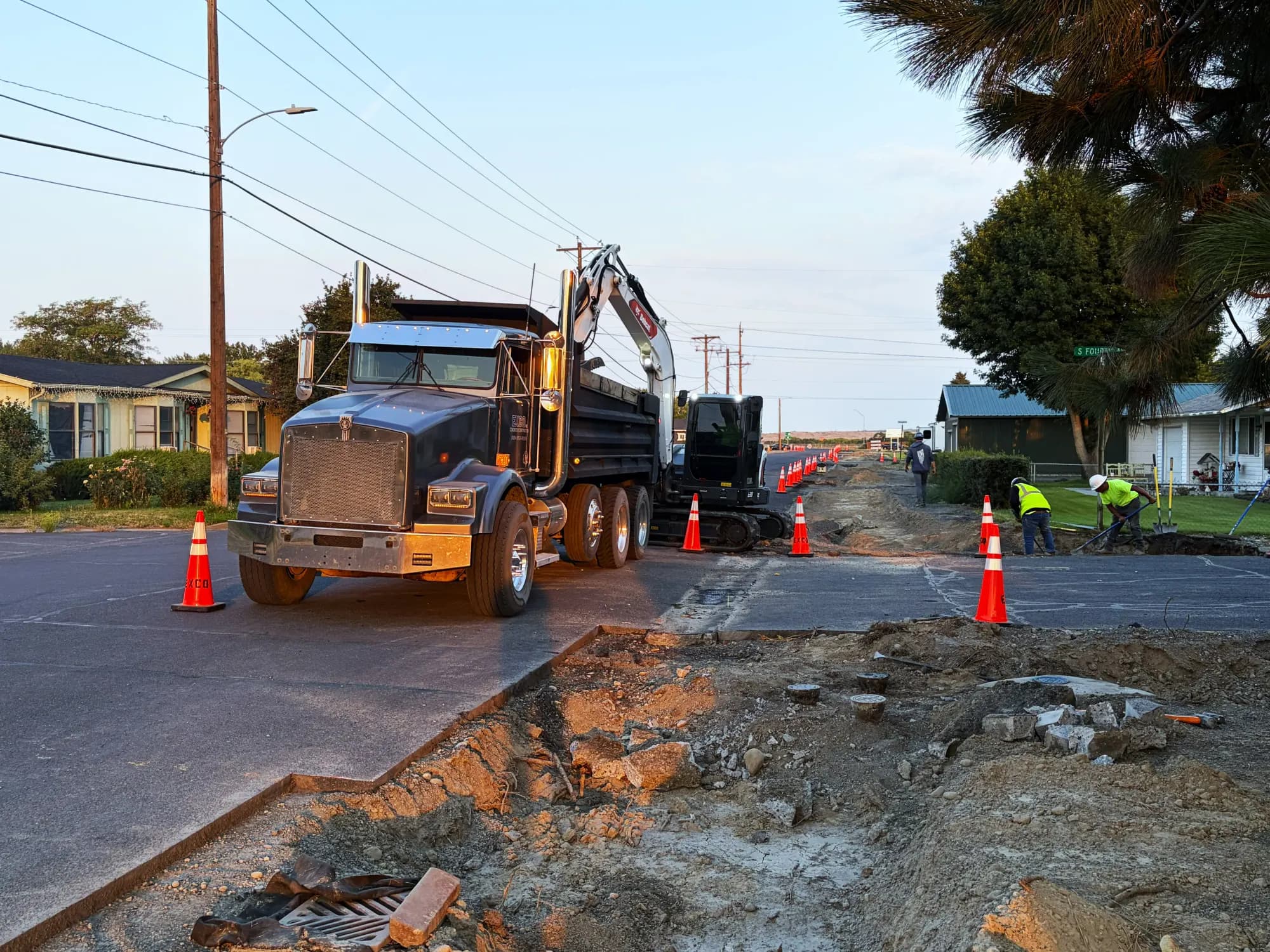 Dump truck and excavator hauling material along a street trench