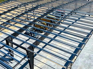 Elevated view across structural steel roof framing and construction equipment